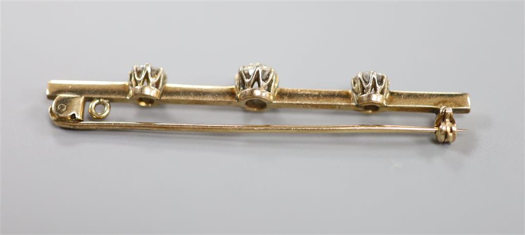 A yellow metal and three stone diamond set bar brooch, 58mm, gross 4.9 grams, set with one oval cushion and two round cut stones.